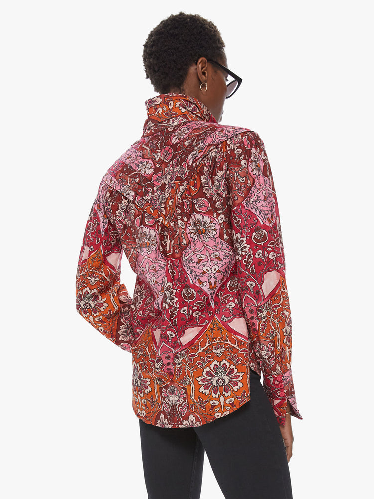 Back view of a woman wearing a long sleeve blouse featuring a red and orange floral print, a cropped flowy body, and a high collar.