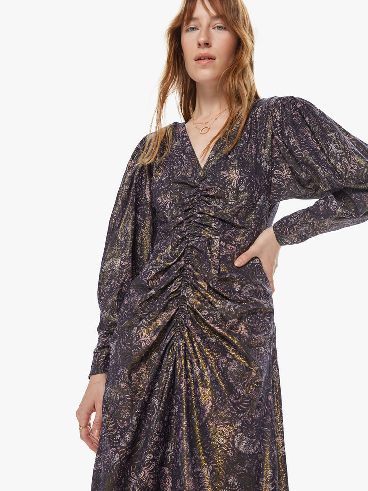 Front close up view of a woman wearing a long sleeve maxi dress featuring a dark paisley print with a gold shimmer, billowed sleeves, and a rouched center seam.