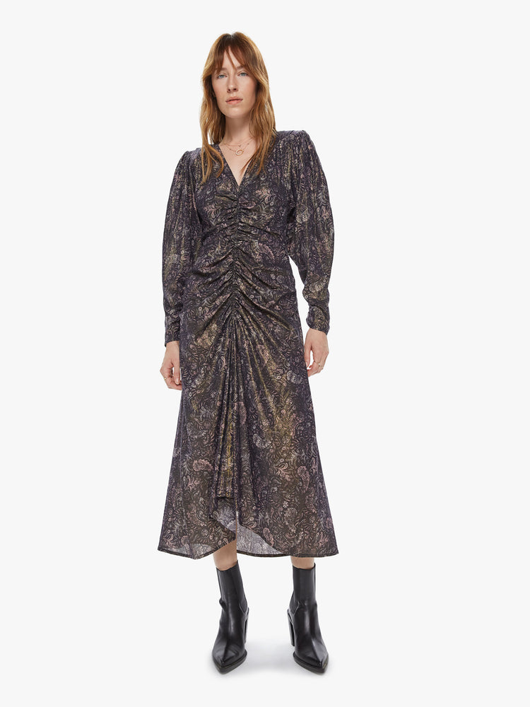 Front view of a woman wearing a long sleeve maxi dress featuring a dark paisley print with a gold shimmer, billowed sleeves, and a rouched center seam.
