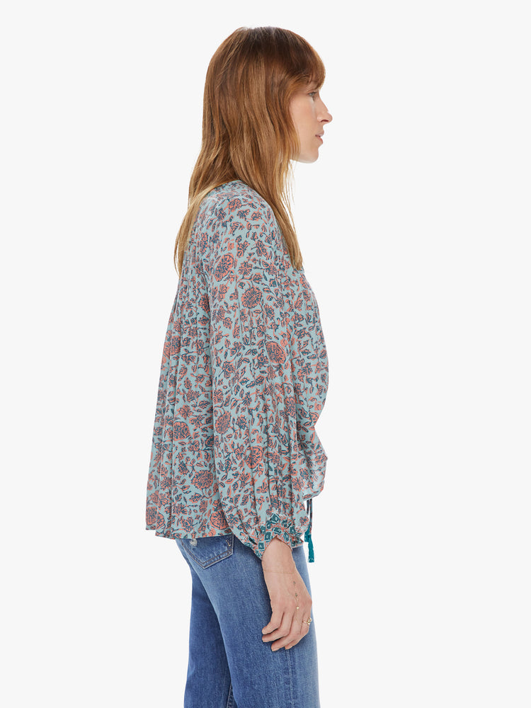 Side view of a woman wearing a flowy top featuring long sleeves, a deep v-neck with a tie, and a pale green and coral floral print.