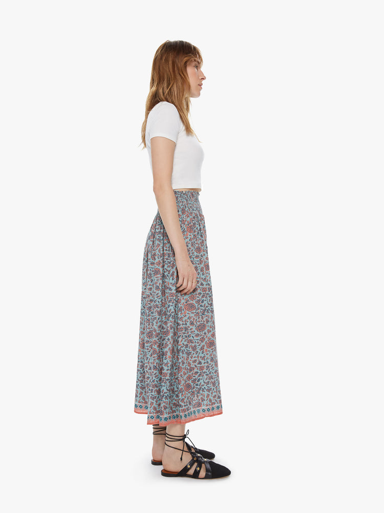 Side view of a woman wearing a flowy skirt featuring an elastic high rise and a pale green and coral floral print.