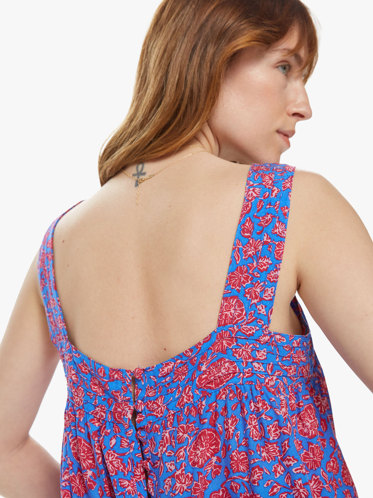 Back close up view of a woman wearing a sleeveless top featuring a slightly cropped body, thick straps, buttons on the back and a blue and pink floral print.