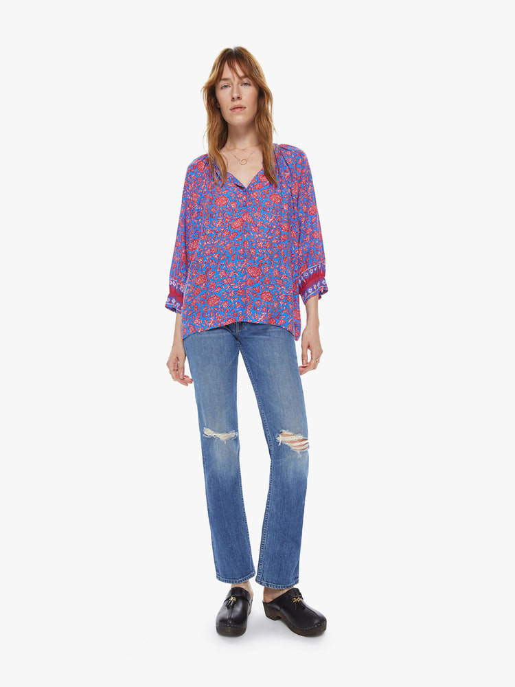 Front full body view of a woman wearing a flowy button down top featuring 3/4 length sleeves and a blue and pink floral print.