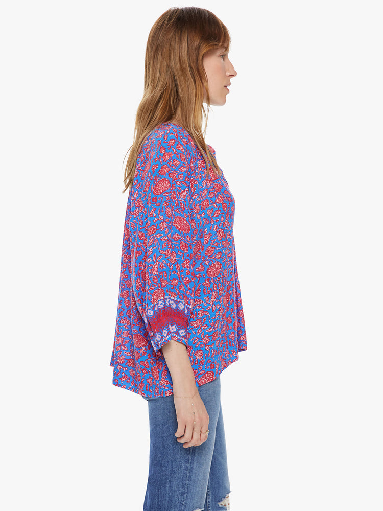 Side view of a woman wearing a flowy button down top featuring 3/4 length sleeves and a blue and pink floral print.