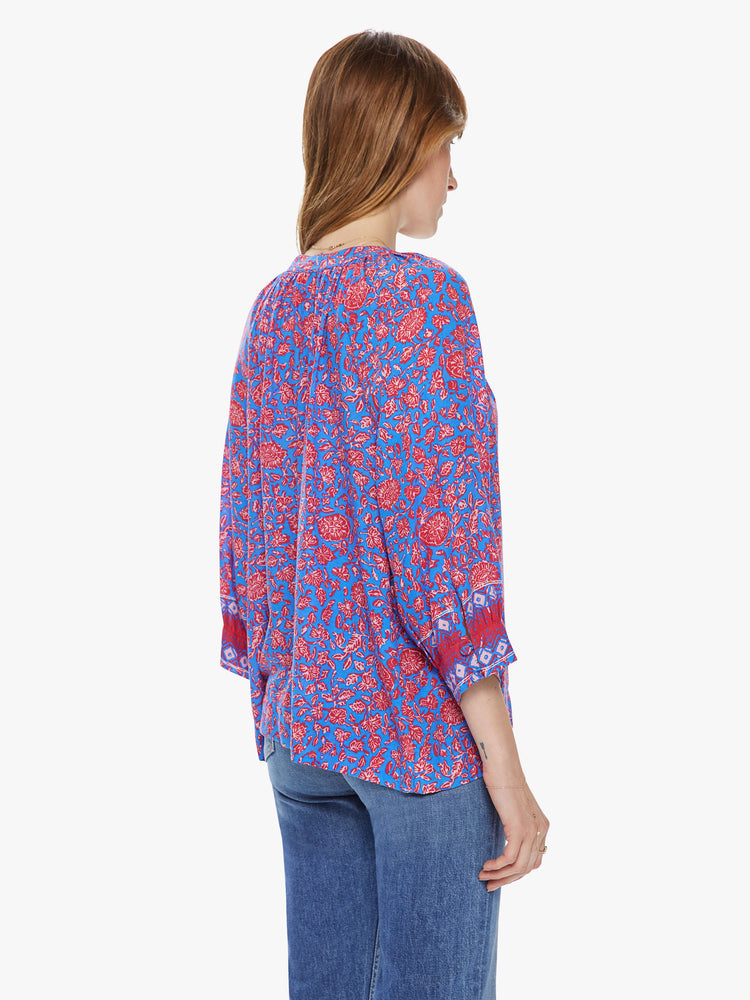 Back view of a woman wearing a flowy top featuring 3/4 length sleeves and a blue and pink floral print.
