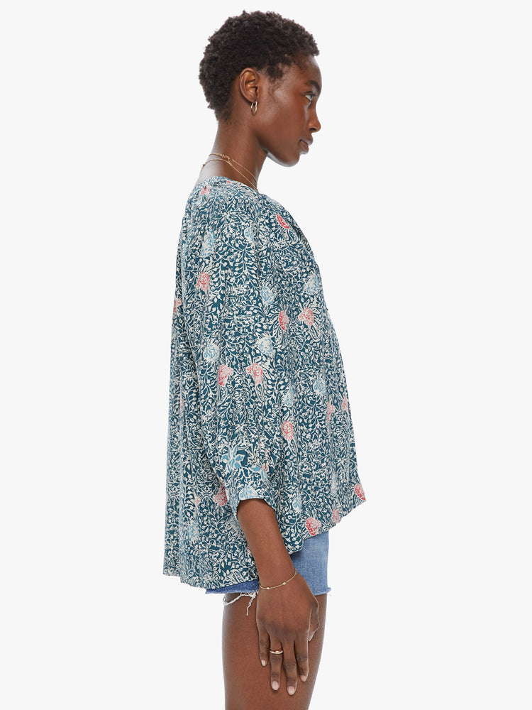 Side view of a woman wearing a 3/4 long sleeve blouse featuring a button v neck, a flowy fit, and a green floral print.