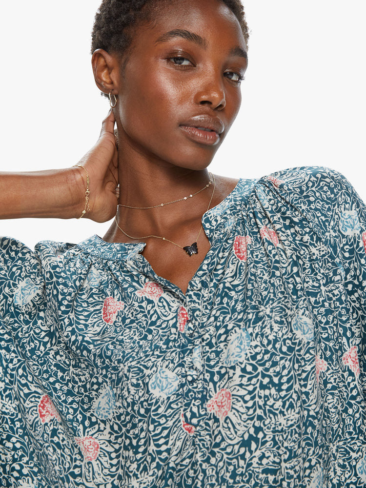 Front close up view of a woman wearing a 3/4 long sleeve blouse featuring a button v neck, a flowy fit, and a green floral print.