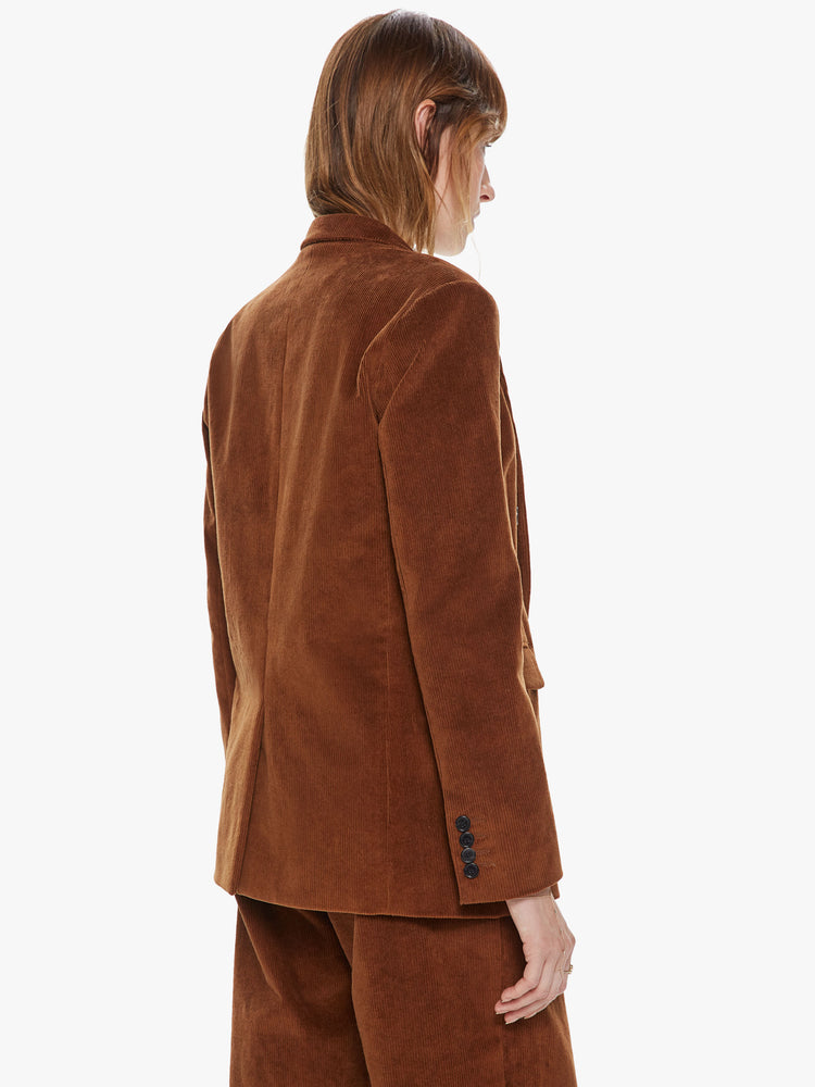 Back view of a woman wearing a brown corduroy blazer featuring two flap pockets, shoulder pads and an oversized lapel. 