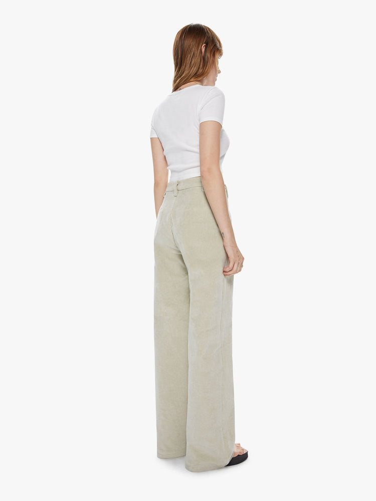Back view of a woman wearing cream colored corduroy pants featuring a high, pleated waist and wide straight legs.