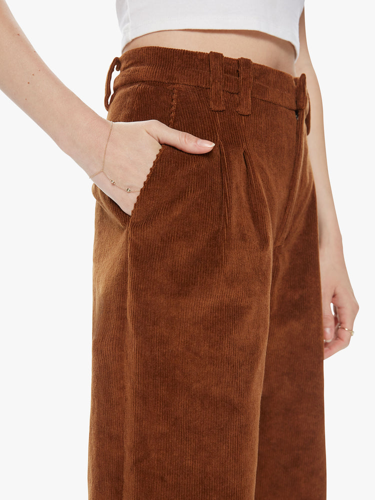 Side close up view of a woman wearing dark brown corduroy pants featuring a high, pleated waist and wide straight legs.