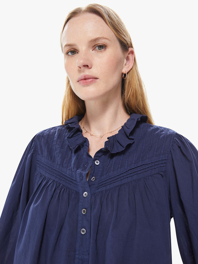 Front detail view of a women's navy blue long sleeve blouse with a button-front placket and ruffle neckline