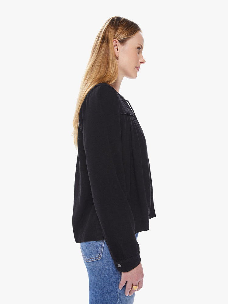 Side view of a women's black long sleeve blouse, featuring a flowy fit and a keyhole neck with tie.