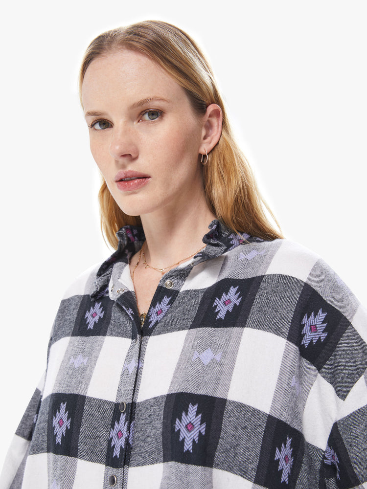 Front close up view of a women's long sleeve button down featuring a ruffled collar, a black and white gingham print with purple details, and a loose oversized fit.