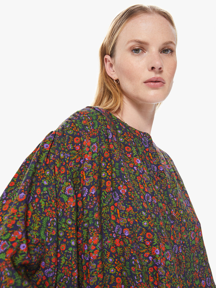 Side close up view of a women's button down blouse featuring a colorful floral print, a crew neck collar, billow sleeves, and a loose fit.