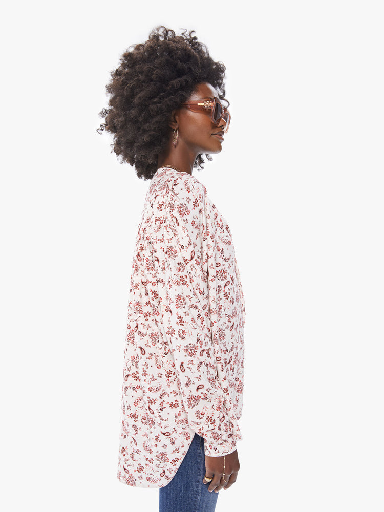 Side view of a womans long sleeve blouse, featuring an off white with red floral print, billowed sleeves, and a v neck with tie.