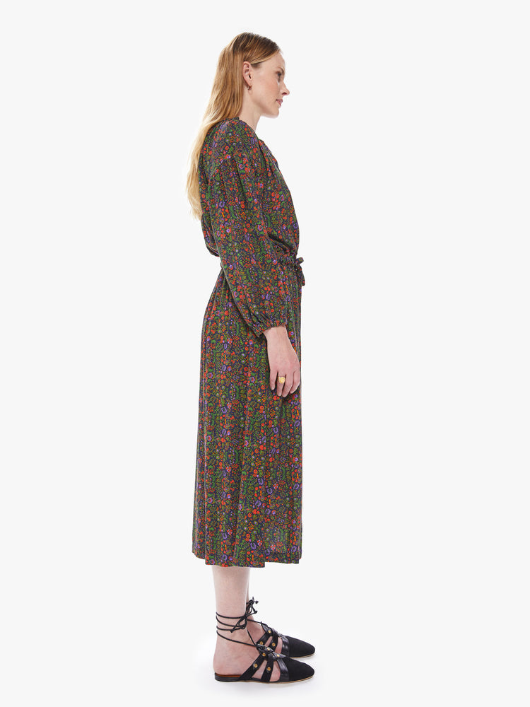 Side view of a women's long sleeve dress featuring a dark floral print, buttoned v neck, a waist tie, and a flowy fit.