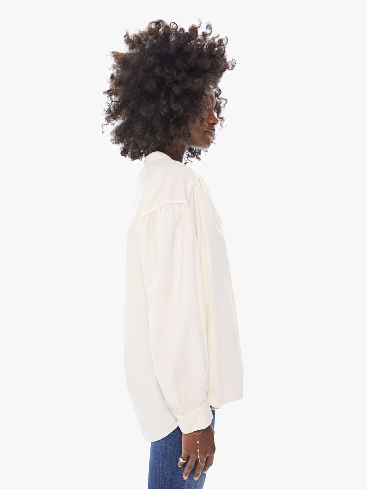 Side view of a women's long sleeve blouse in a thin corduroy fabric, featuring billow sleeves, rouched details along the shoulder, and button down collar.