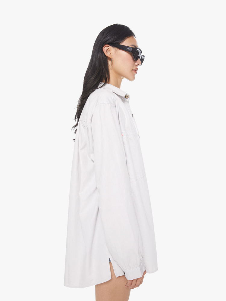 Side view of a woman wearing white button down shirt featuring an oversized fit, and pleated details along the shoulder hem.