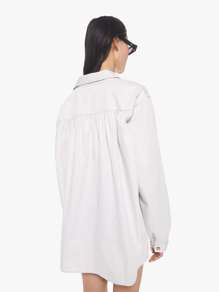 Back view of a woman wearing white button down shirt featuring an oversized fit, and pleated details along the shoulder hem.