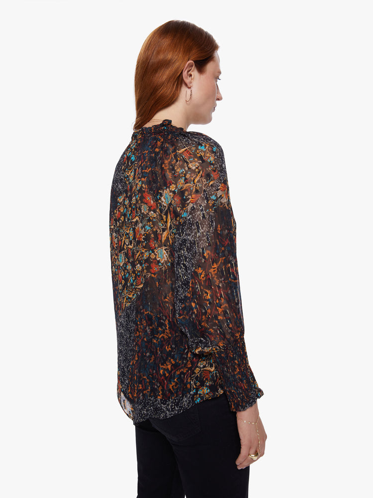 Back view of a womens dark printed button down blouse featuring loose long sleeves with smocked cuffs and a flowy fit.