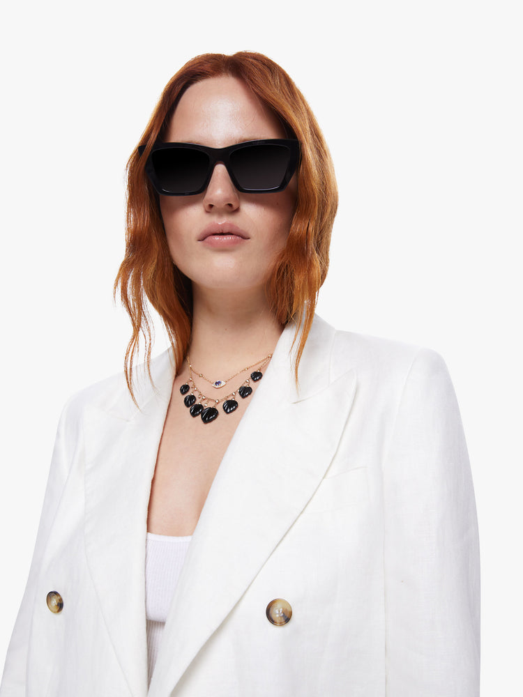 A detail view of a woman wearing an off-white blazer with angled hem and buttons