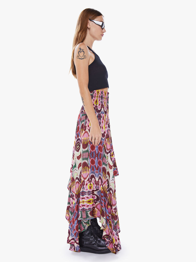 A side view of a woman wearing a colorful, abstract print, pink skirt with an uneven hemline