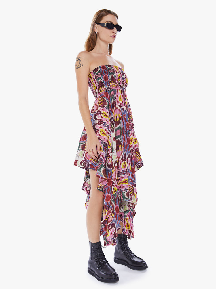 A side view of a woman wearing a colorful, abstract print, pink skirt with an uneven hemline as a dress