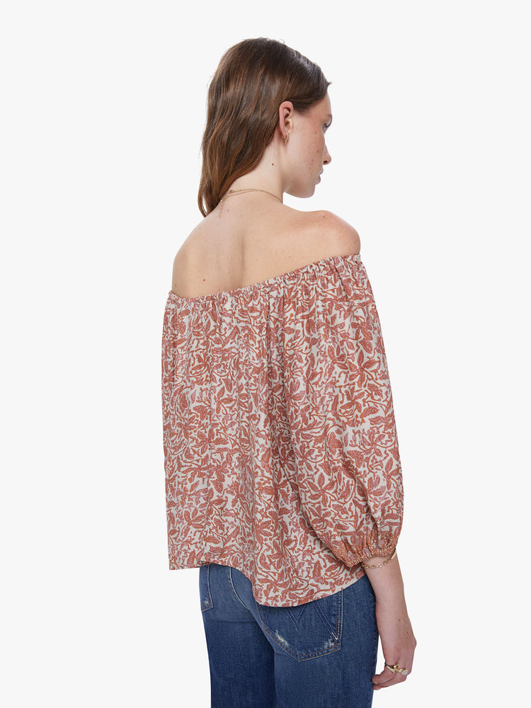 A back view of a woman wearing a delicate orange and cream floral print top with an elastic neckline off the shoulders.