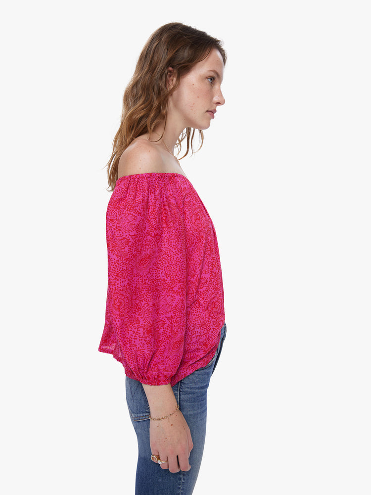 A side view of a woman wearing a raspberry-colored, floral print top with an elastic neckline off the shoulders.
