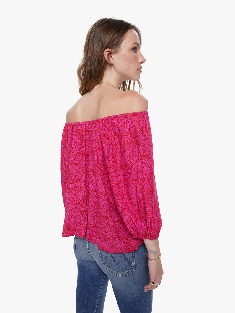 A back view of a woman wearing a raspberry-colored, floral print top with an elastic neckline off the shoulders.