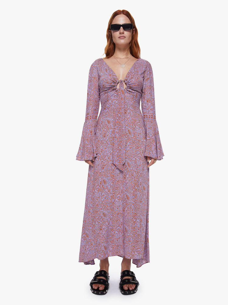 A front view of a woman wearing an orchid-purple and rust floral print, full length dress with bell sleeves and keyhole neckline.
