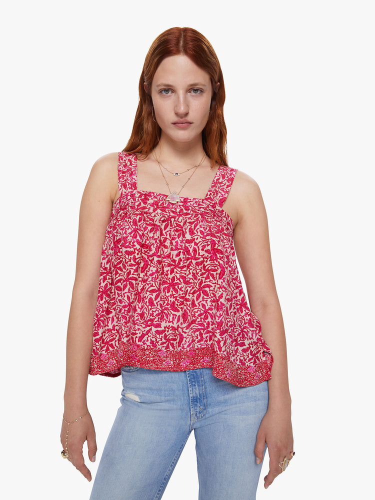 Front view of a woman wearing a flowy pink floral print top with detailed straps and buttons in the back