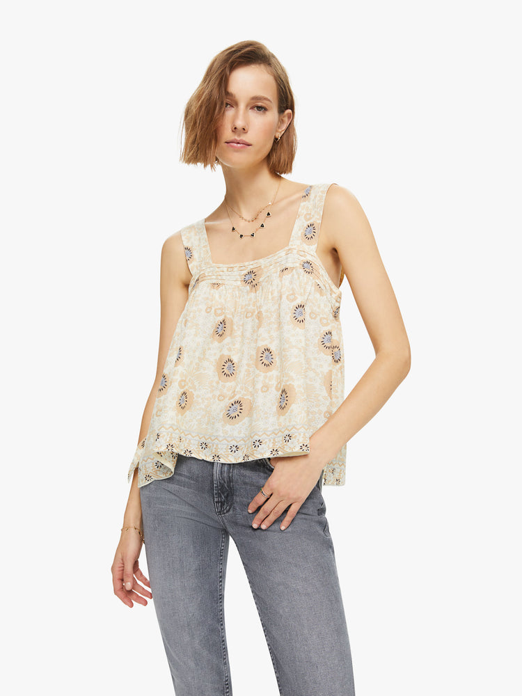 Front view of a woman wearing a flowy sandy-hued floral print top with detailed straps and buttons in the back.