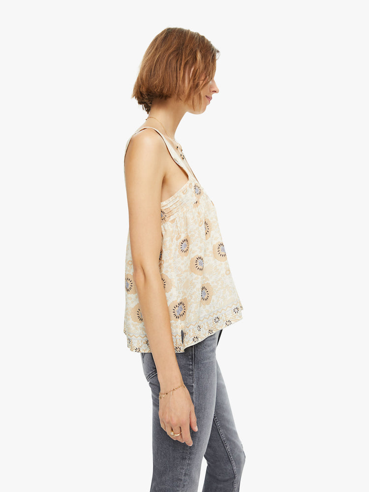 Side view of a woman wearing a flowy sandy-hued floral print top with detailed straps and buttons in the back.