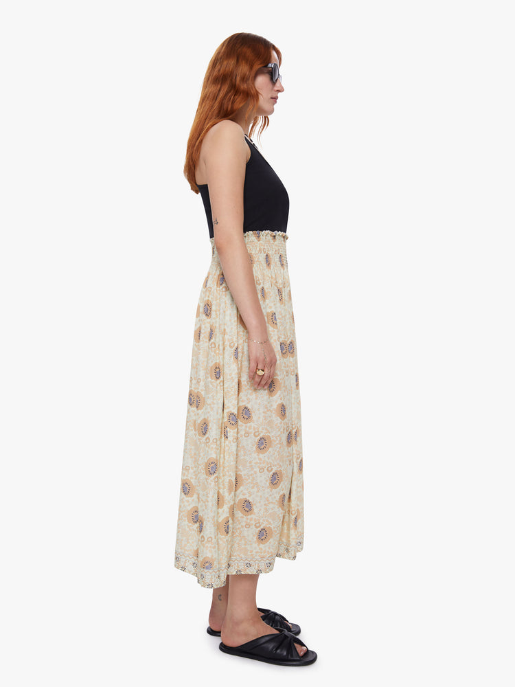 Side view of a woman wearing a beige floral maxi skirt with a smocked waistband and loose flowy fit