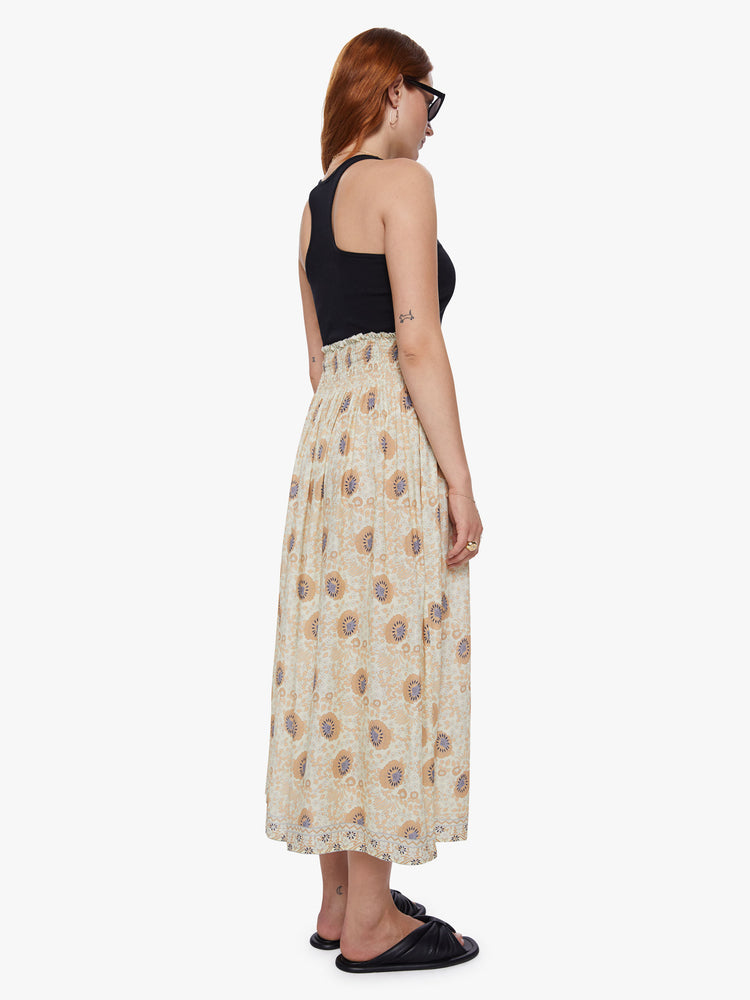 Back view of a woman wearing a beige floral maxi skirt with a smocked waistband and loose flowy fit