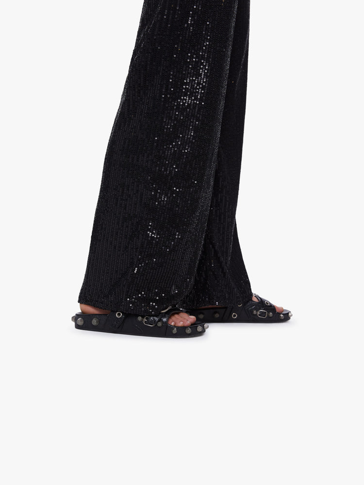 Side close up view of a womens wide leg pants featuring black sequins, a high rise, and a flowy fit.