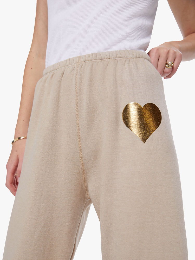 Detail view of a woman wearing khaki sweatpants with a gold heart on upper left leg