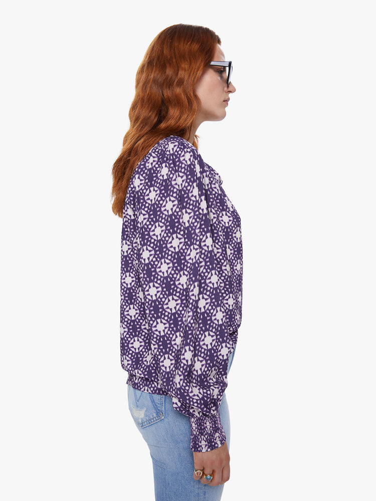 Side view of a womens v neck blouse featuring a white and purple print, billow sleeves, and a flowy fit.