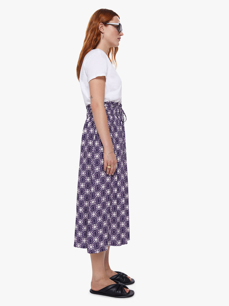 Side view of a womens mid length skirt featuring a purple and white print, a rouched high waist, and a flowy fit.