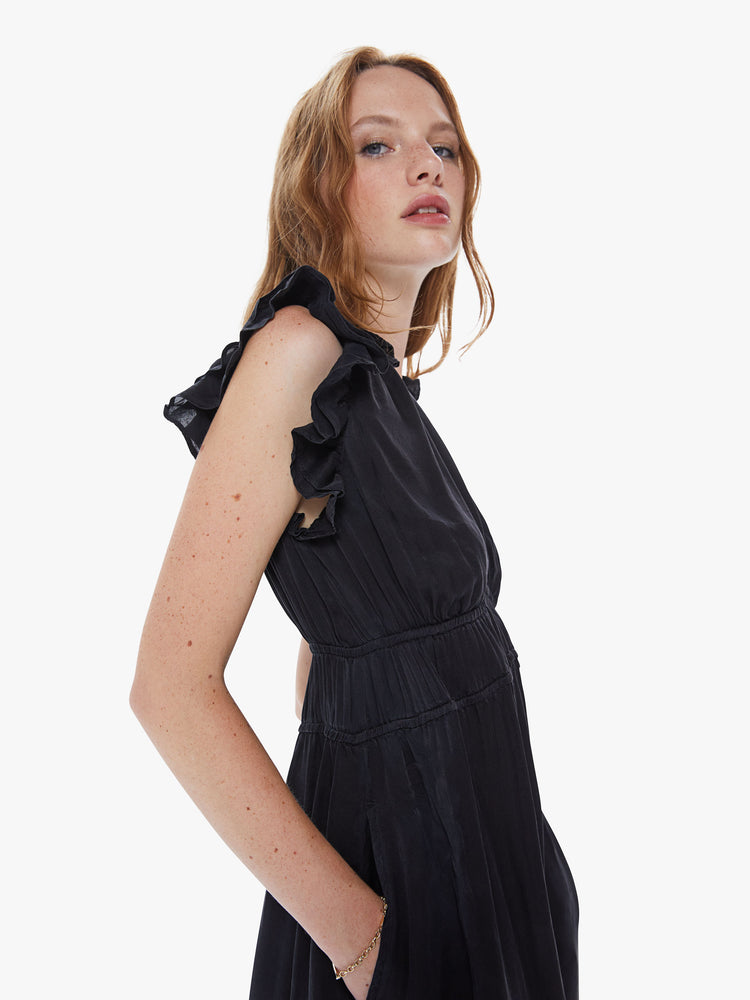 Side close up view of a womens black midi dress, featuring sleeveless ruffles, concealed side pockets, a deep v neck, and a smocked high waist.