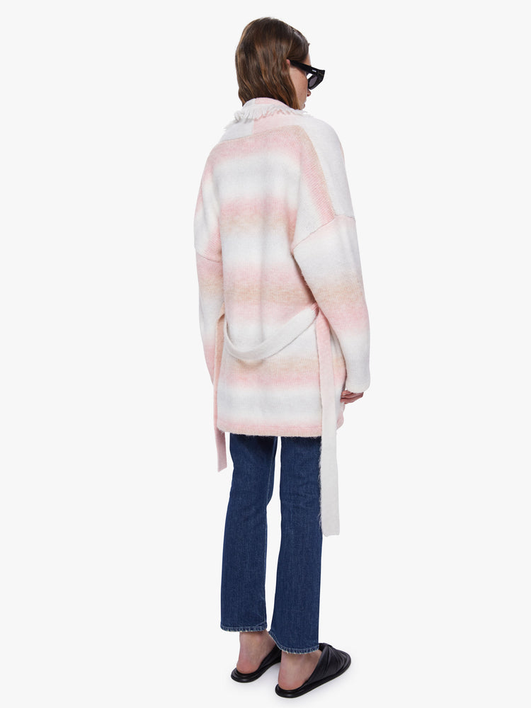 Back view of a womens long cardigan, featuring soft pink and white stripes, dropped sleeves, fringe trim, and a belted tie.