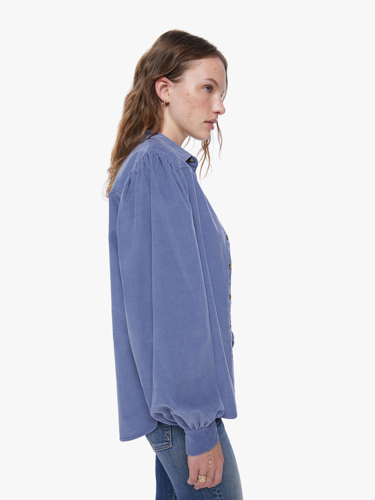 Side view of a womens blue button down shirt, featuring a chest pocket and long billow sleeves.