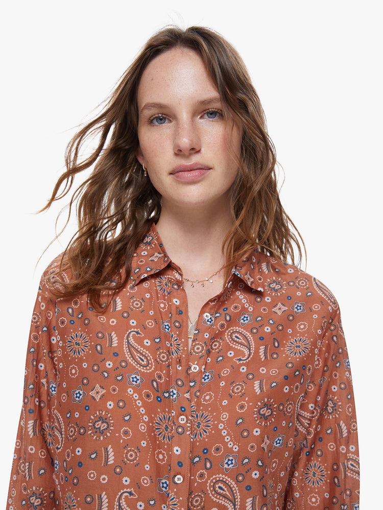 A detail view of a woman wearing a burnt orange button up shirt with paisley print