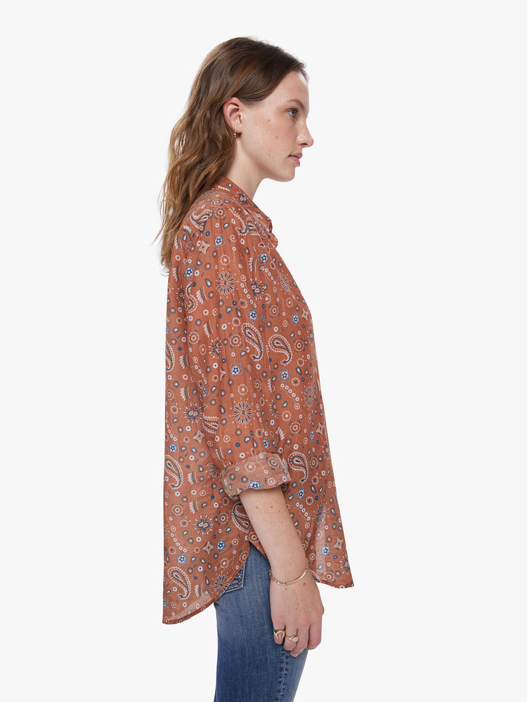 A side view of a woman wearing a burnt orange button up shirt with paisley print