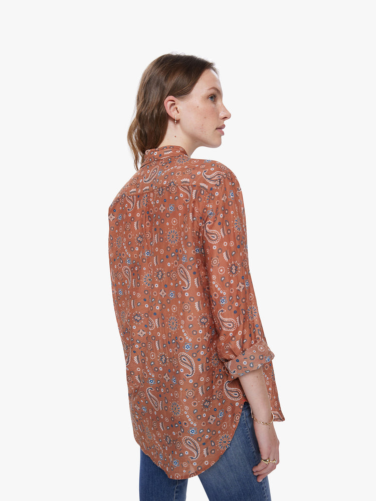 A back view of a woman wearing a burnt orange button up shirt with paisley print