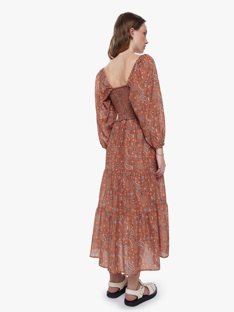 A back view of a woman wearing a burnt orange dress with a paisley print and 3/4 length balloon sleeves