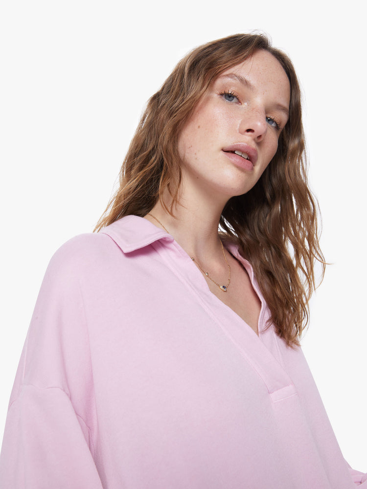 A detail view of a woman wearing a light pink sweatshirt with a deep v, collared neckline