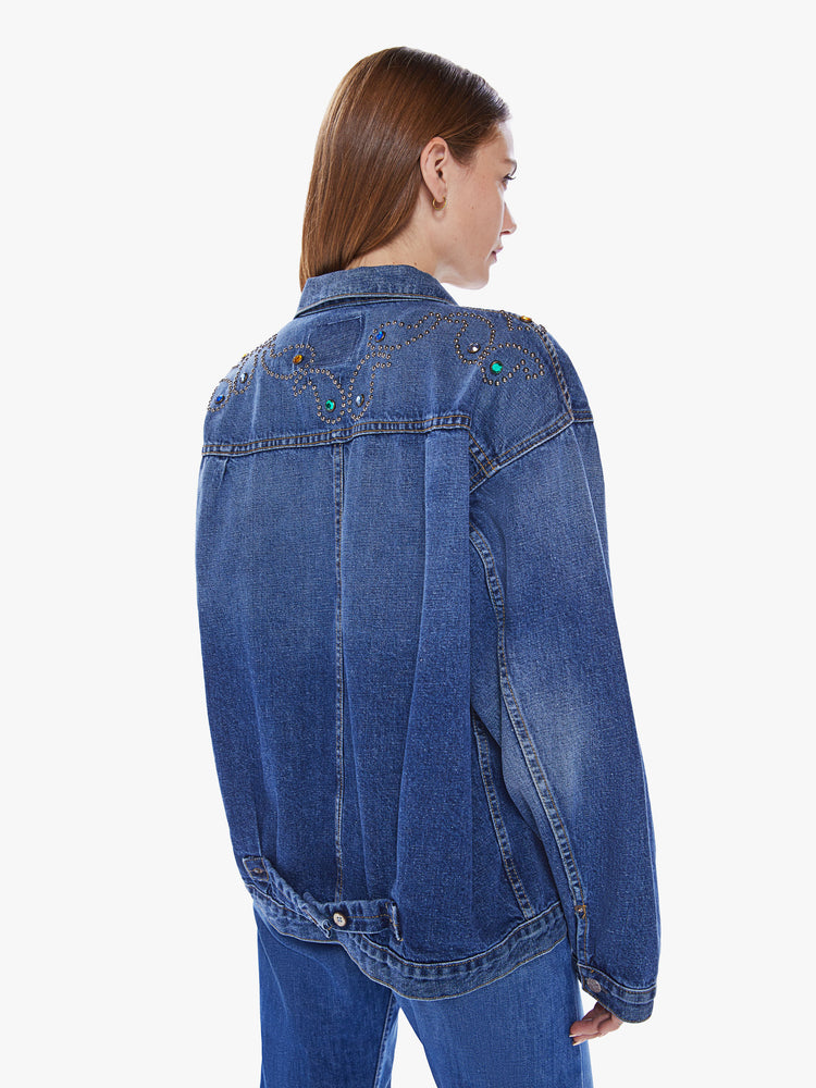 A back view of a woman wearing a dark blue denim jacket with studded paisley detail