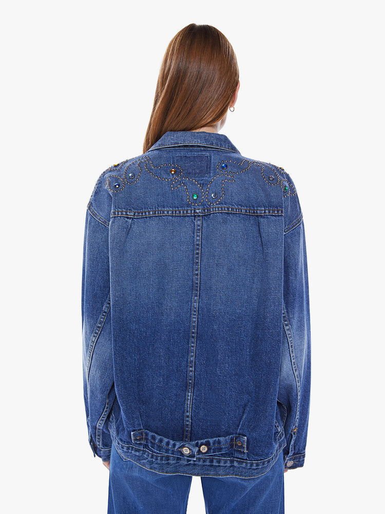 A back view of a woman wearing a dark blue denim jacket with studded paisley detail